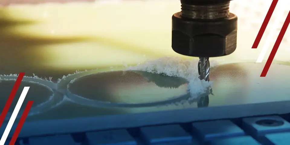 A drill bit cuts circular shapes into a pale, textured surface using a CNC machine. The process produces small piles of debris.