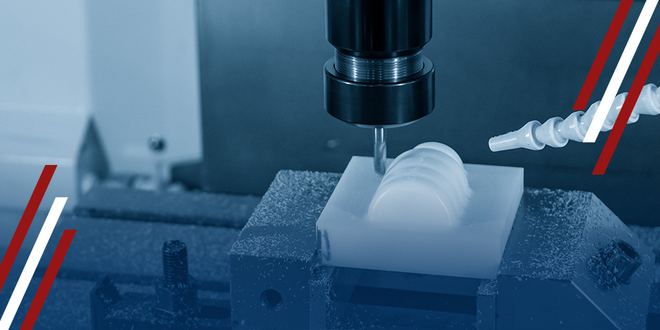 A CNC milling machine cuts a white block of material. The machine is in a dark-blue industrial setting.