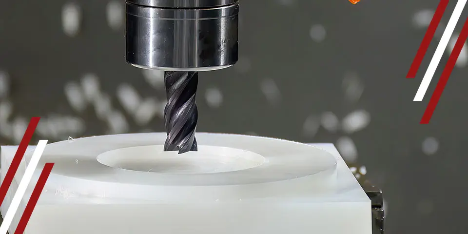 A drill bit cuts into a white cylindrical object. White shavings fly off. The setting is an industrial machine shop.