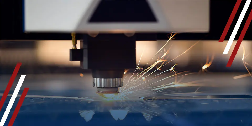 A laser cutter cuts a metal sheet, producing bright sparks; the process takes place in an industrial setting.