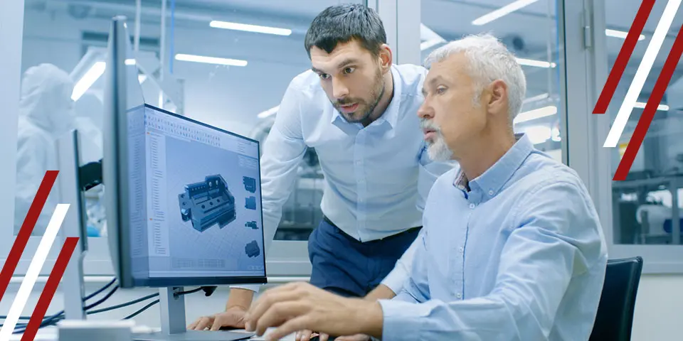 Two men review a 3D CAD model on a computer screen in a modern factory setting.