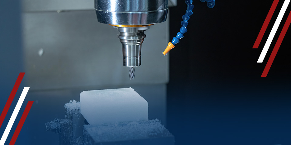 A CNC mill's drill bit carves a white block of material, amidst machining debris. The process occurs within a dark, industrial setting.