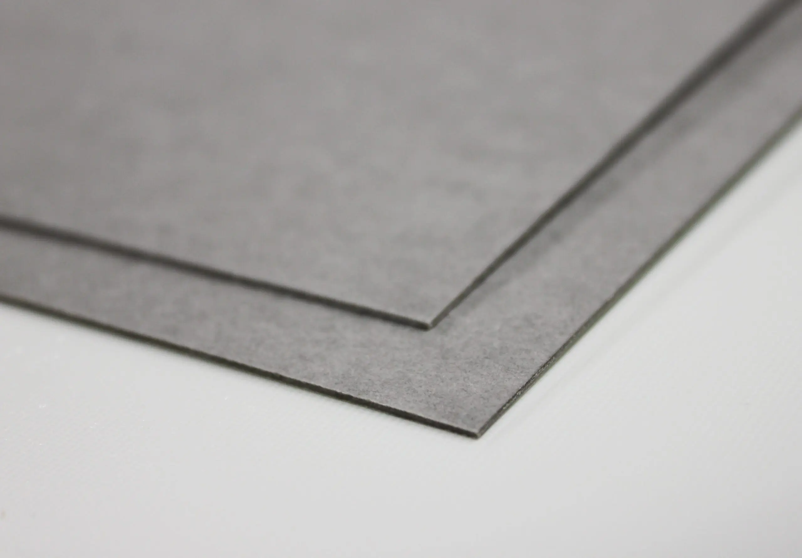Two gray rectangular sheets of material are stacked, angled on a white surface.