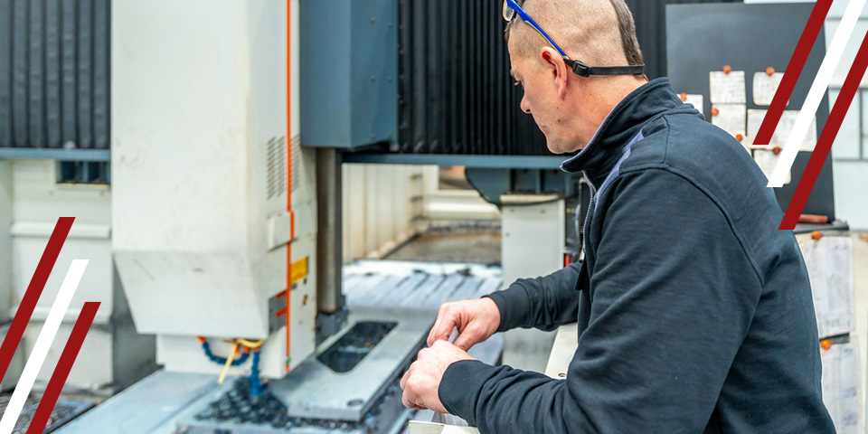 A man operates a large industrial machine in a factory. He is manipulating a piece of metal near the machine's cutting head.